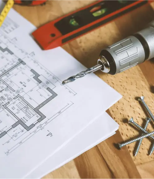 Blueprints, drill, screws, and woodworking tools on a table symbolizing the design and construction process of live edge tables in Ottawa.